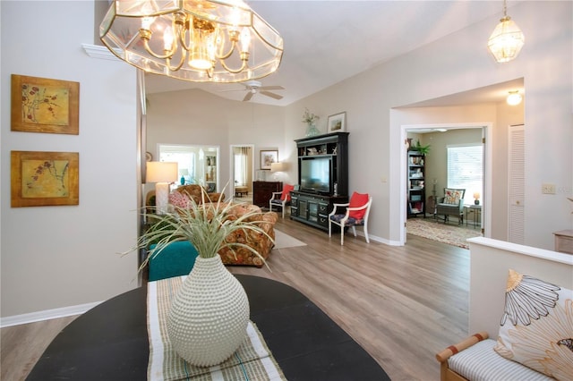 living area featuring baseboards, lofted ceiling, wood finished floors, and ceiling fan with notable chandelier