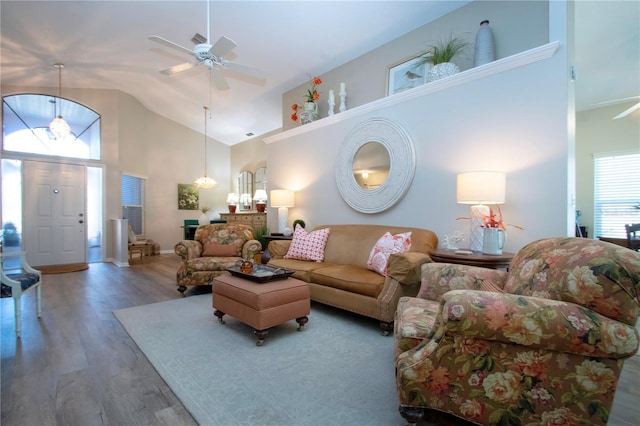 living area with ceiling fan with notable chandelier, high vaulted ceiling, and wood finished floors