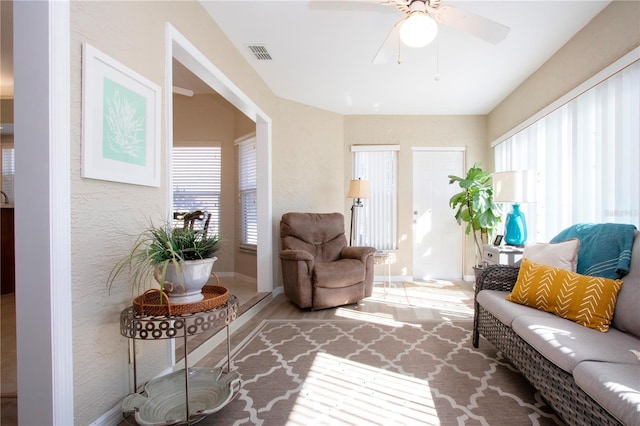 living area with visible vents, ceiling fan, baseboards, and a textured wall