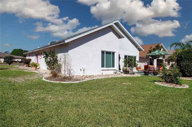 back of property with stucco siding, a patio, and a lawn