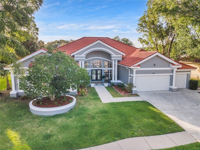 mediterranean / spanish-style home featuring an attached garage, concrete driveway, a tiled roof, french doors, and a front lawn