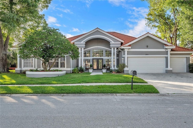 view of front of house with stucco siding, a front lawn, french doors, concrete driveway, and a garage