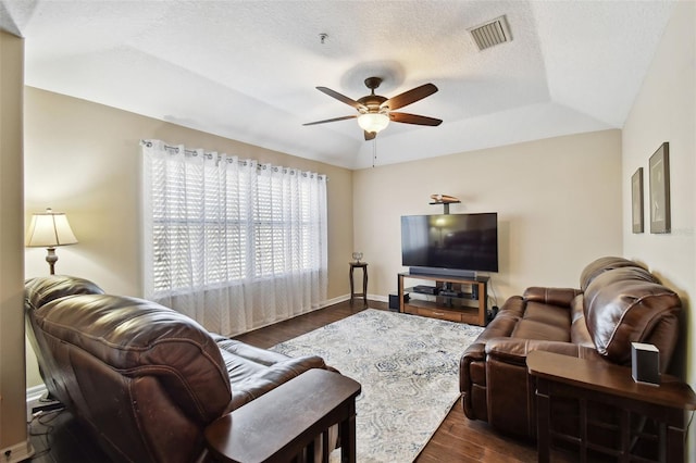 living area with dark wood-style flooring, visible vents, baseboards, a ceiling fan, and a raised ceiling