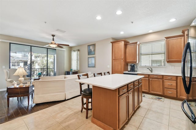 kitchen with light tile patterned floors, brown cabinetry, a breakfast bar, open floor plan, and a sink