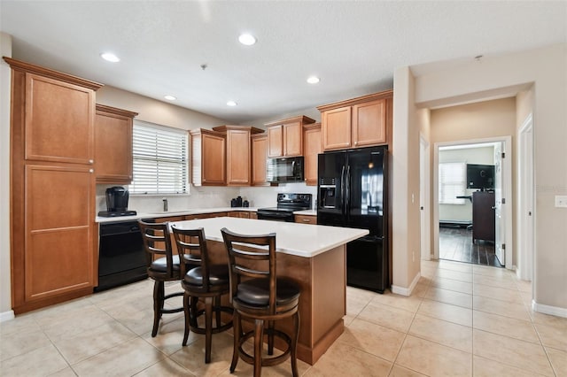 kitchen with a kitchen island, light countertops, black appliances, a sink, and light tile patterned flooring