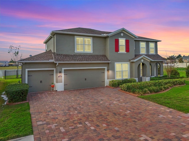 traditional-style home with an attached garage, fence, decorative driveway, stucco siding, and a front lawn