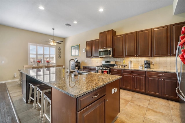 kitchen featuring a sink, a kitchen breakfast bar, appliances with stainless steel finishes, backsplash, and a center island with sink