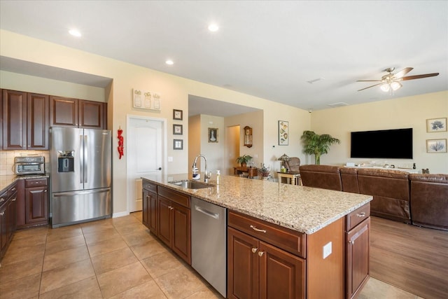 kitchen featuring a center island with sink, decorative backsplash, appliances with stainless steel finishes, open floor plan, and a sink