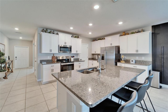 kitchen with light tile patterned floors, stainless steel appliances, an island with sink, and a sink