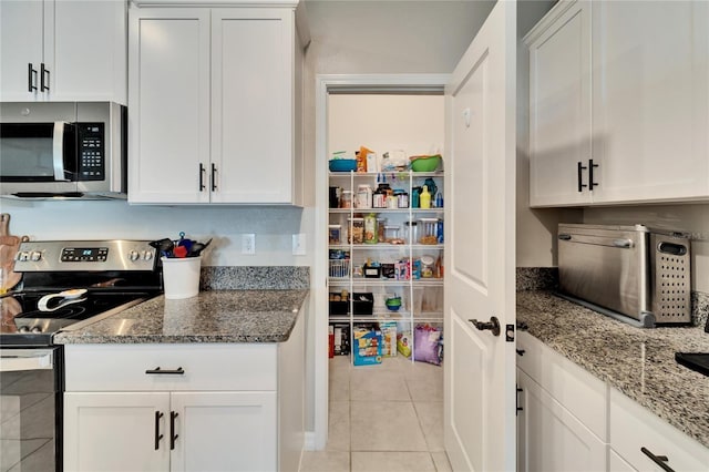 kitchen with white cabinets, light tile patterned floors, dark stone counters, and stainless steel appliances