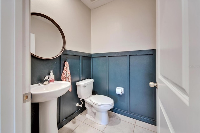 bathroom featuring a wainscoted wall, a decorative wall, toilet, a sink, and tile patterned floors