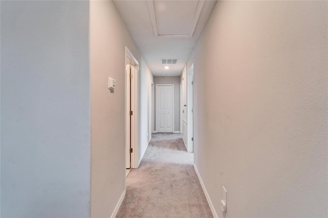 hallway with baseboards, visible vents, and light colored carpet