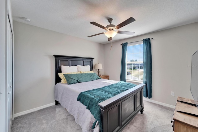 bedroom featuring light carpet, ceiling fan, a textured ceiling, and baseboards