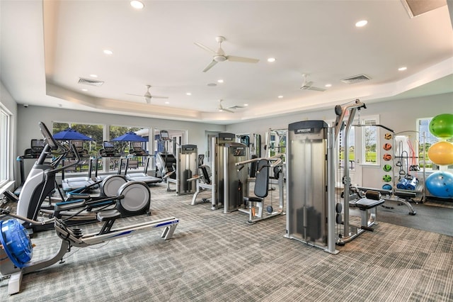 exercise room with a tray ceiling, recessed lighting, visible vents, and a healthy amount of sunlight