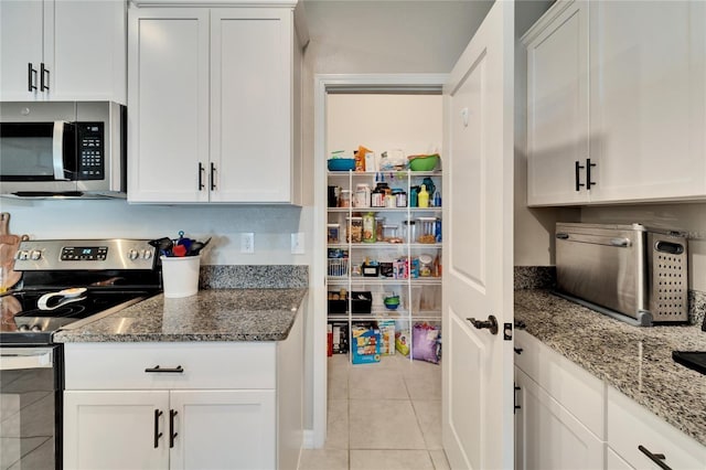 kitchen featuring light tile patterned flooring, dark stone countertops, white cabinetry, and stainless steel appliances
