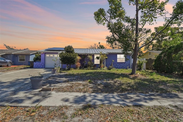 ranch-style house with an attached garage, roof mounted solar panels, a standing seam roof, metal roof, and driveway