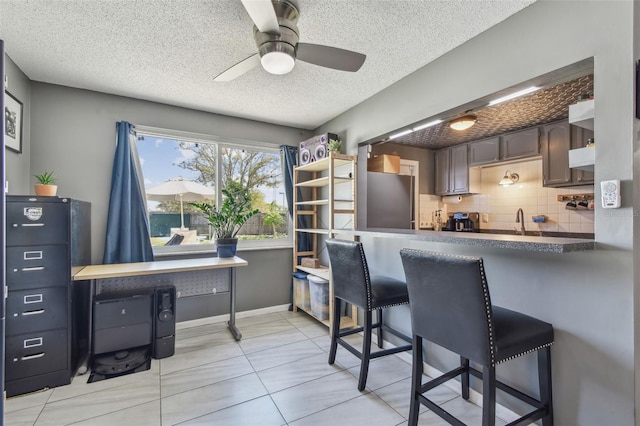 kitchen with dark countertops, a kitchen breakfast bar, freestanding refrigerator, a textured ceiling, and backsplash