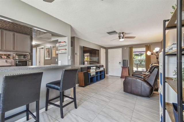 kitchen with a toaster, ceiling fan, a textured ceiling, and a breakfast bar area