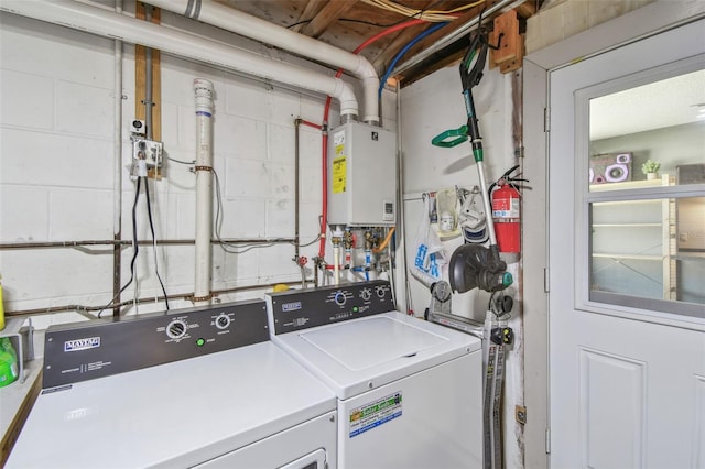 clothes washing area featuring concrete block wall, washing machine and dryer, and tankless water heater