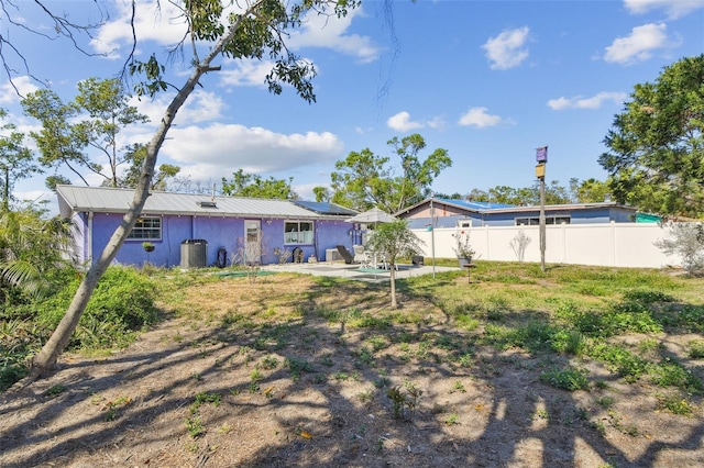 rear view of house with stucco siding, fence, metal roof, and a patio