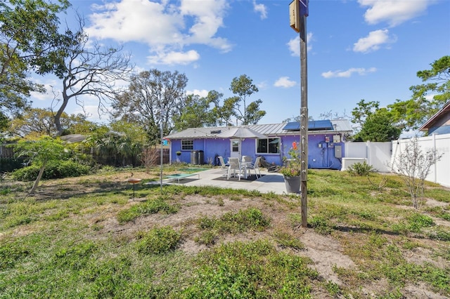 rear view of property featuring a fenced backyard, metal roof, a gate, a patio area, and roof mounted solar panels