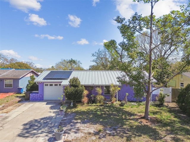 ranch-style home with metal roof, a garage, fence, concrete driveway, and roof mounted solar panels