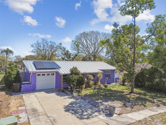 ranch-style house featuring solar panels, a standing seam roof, metal roof, a garage, and driveway