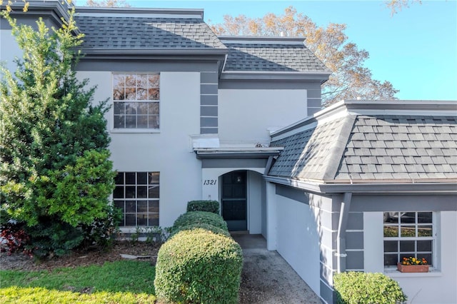 view of front of property featuring a shingled roof, mansard roof, and stucco siding