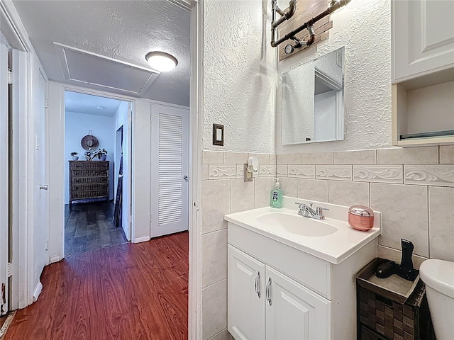 bathroom featuring a textured ceiling, toilet, wood finished floors, vanity, and tile walls