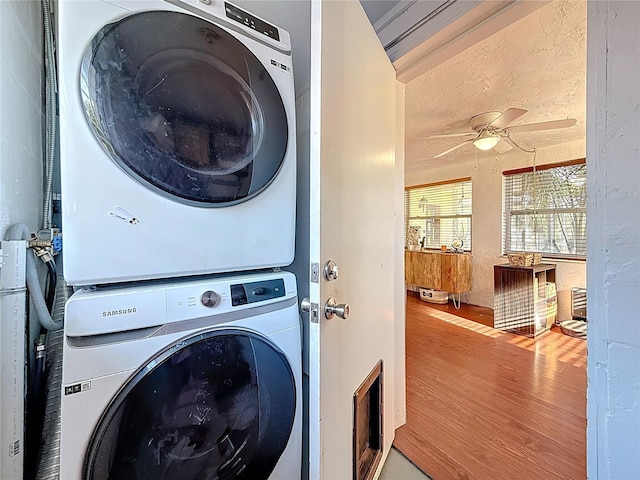 clothes washing area featuring laundry area, a ceiling fan, stacked washer / dryer, wood finished floors, and a textured ceiling