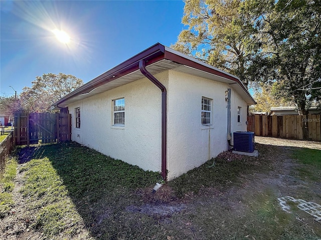 view of property exterior with central AC unit, fence, and stucco siding