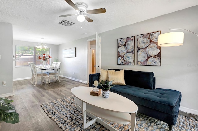 living area with a textured ceiling, wood finished floors, visible vents, and baseboards