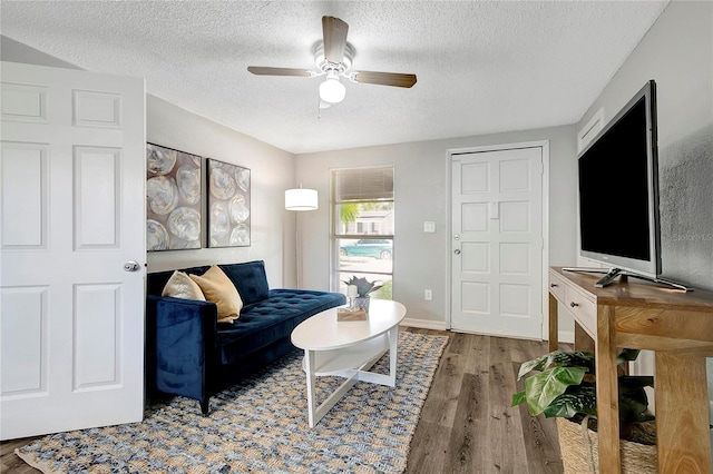 living room featuring ceiling fan, a textured ceiling, baseboards, and wood finished floors