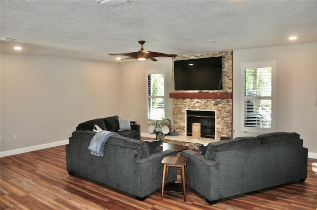 living room featuring a textured ceiling, a stone fireplace, dark wood-type flooring, and plenty of natural light