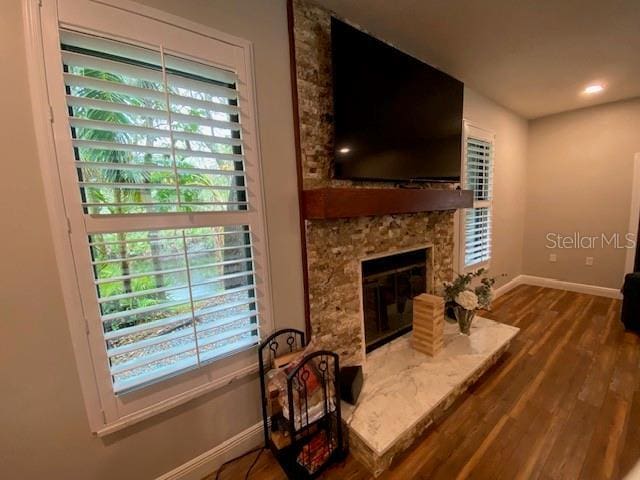 living room with a stone fireplace, baseboards, and wood finished floors