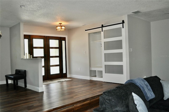 foyer entrance with french doors, a barn door, dark wood-type flooring, and baseboards