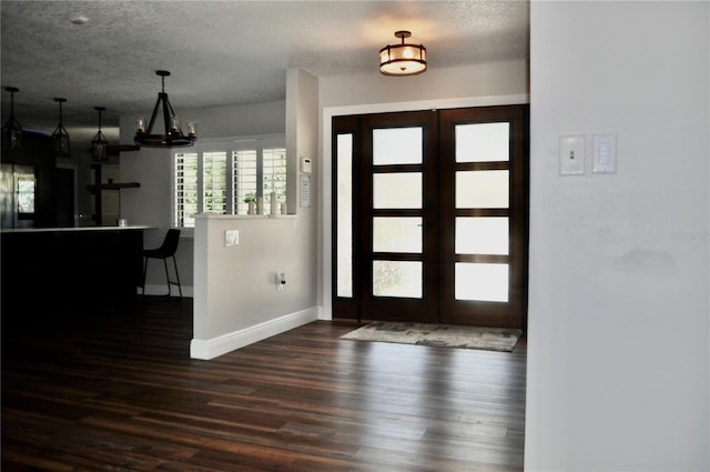 foyer entrance featuring baseboards, wood finished floors, a textured ceiling, french doors, and a chandelier