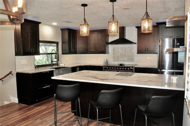 kitchen featuring tasteful backsplash, dark wood finished floors, light stone counters, stainless steel appliances, and wall chimney range hood