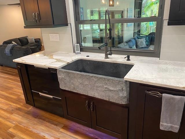 kitchen with light wood-type flooring, light stone countertops, dark brown cabinetry, and a sink