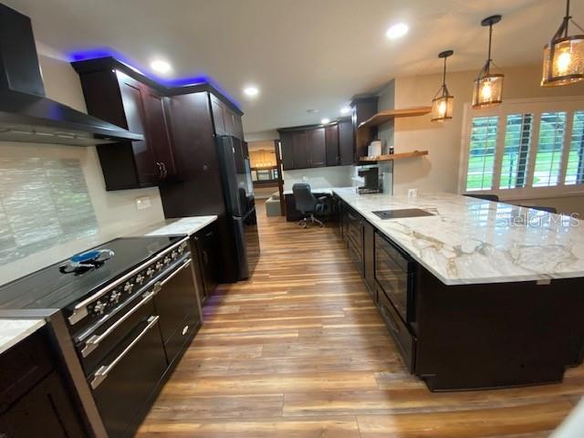 kitchen featuring light wood finished floors, wall chimney exhaust hood, open shelves, a peninsula, and black appliances