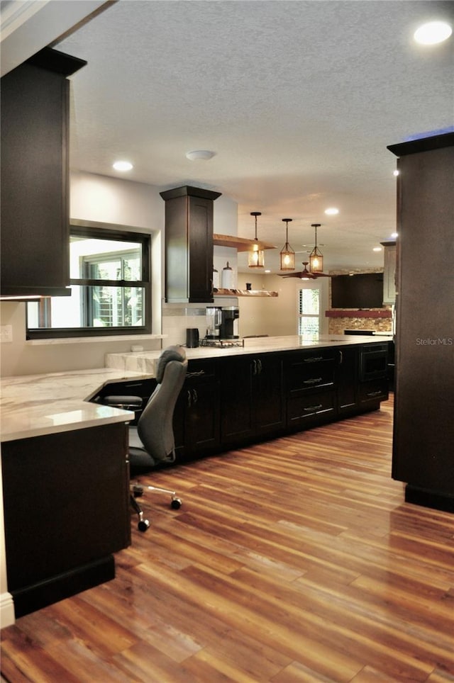 kitchen with dark cabinets, light wood-type flooring, light countertops, and open shelves