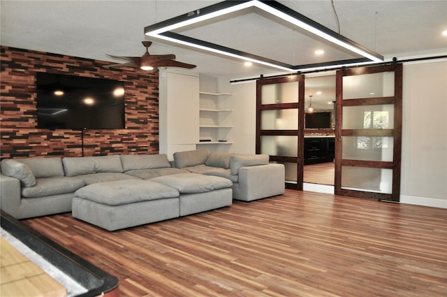 unfurnished living room with a barn door, ceiling fan, and wood finished floors