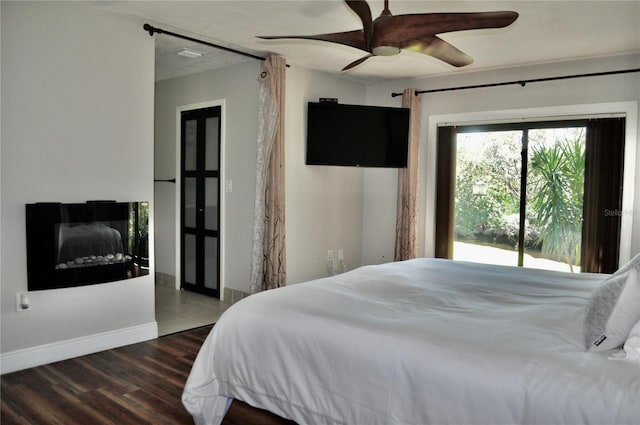 bedroom with a fireplace, ceiling fan, baseboards, and wood finished floors