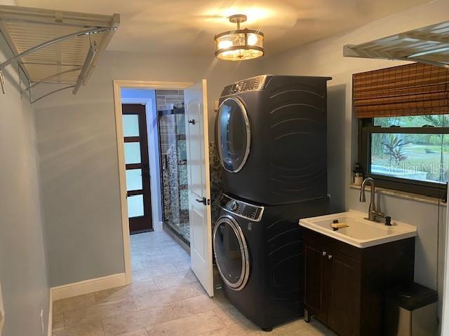 clothes washing area featuring stacked washing maching and dryer, a sink, and baseboards