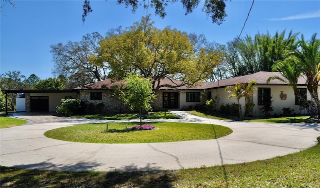 ranch-style home with driveway, a garage, stone siding, a front yard, and stucco siding