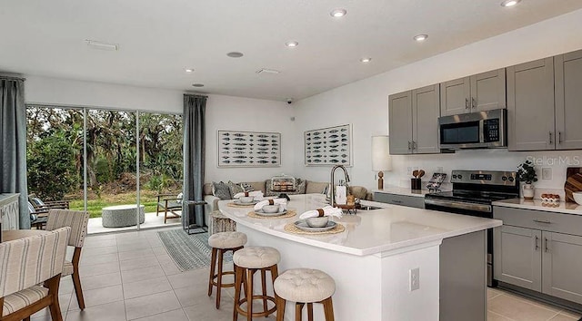 kitchen featuring a kitchen island with sink, stainless steel appliances, light countertops, gray cabinetry, and a sink