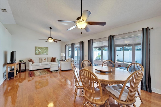 dining area featuring a textured ceiling, visible vents, baseboards, vaulted ceiling, and light wood finished floors