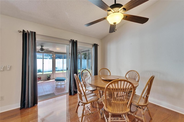 dining space featuring baseboards, a textured ceiling, vaulted ceiling, and light wood-style floors