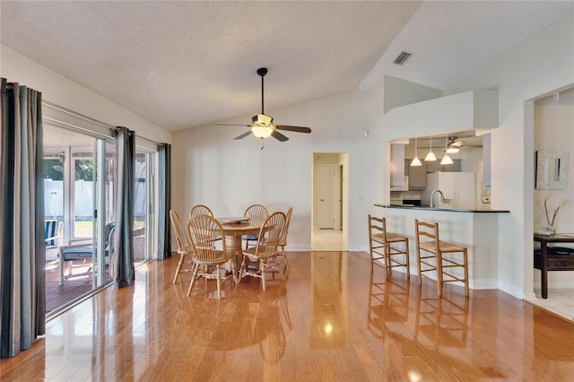 dining space with visible vents, a ceiling fan, lofted ceiling, a textured ceiling, and light wood-style floors