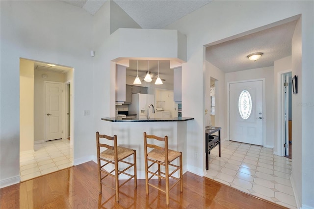 kitchen featuring dark countertops, a breakfast bar, a textured ceiling, light wood-style floors, and white fridge with ice dispenser